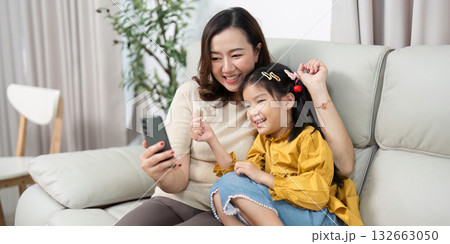 Family Joy and Screen Time. A mother and daughter share a lighthearted moment while looking at a smartphone. Family Joy and Screen Time. A mother and daughter share a lighthearted moment while looking at a smartphone. 132663050