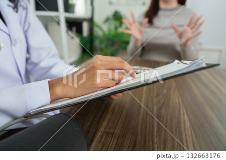 Consultation and Patient Engagement. A doctor attentively takes notes during a patient's consultation, ensuring a thorough examination of health concerns. 132663176