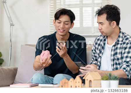Loving LGBTQ couple discussing savings strategies while sitting on a couch at home. Financial planning and budgeting for a secure future in a cozy living space. Loving LGBTQ couple discussing savings strategies while sitting on a couch at home. Financial planning and budgeting for a secure future in a cozy living space. 132663186