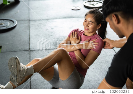 Workout session with personal trainer assisting female client in gym Workout session with personal trainer assisting female client in gym 132663282