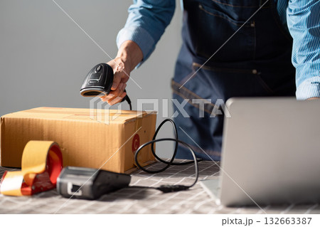 E-commerce entrepreneur scanning a package with a barcode scanner at a workspace, preparing for online selling and shipping. E-commerce entrepreneur scanning a package with a barcode scanner at a workspace, preparing for online selling and shipping. 132663387