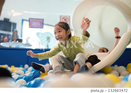 Exciting Slide Adventure. Happy girl sliding down into colorful ball pit, expressing joy and excitement. Exciting Slide Adventure. Happy girl sliding down into colorful ball pit, expressing joy and excitement. 132663472