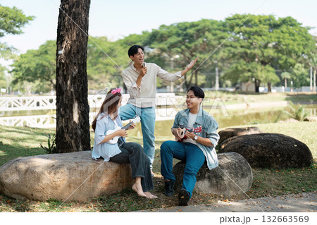 Diverse friends enjoying a musical jam session outdoors in a park, celebrating creativity and friendship under the sun. 132663569