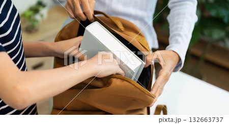 Back to School and Organizing Supplies. Two hands placing books into a backpack for school. 132663737