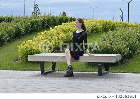 Woman sitting on a bench removing shoes in a park on a sunny day. Woman sitting on a bench removing shoes in a park on a sunny day. 132663911