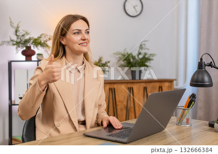 Businesswoman works on laptop shows thumbs up like gesture smiles approves positive results proud up Businesswoman works on laptop shows thumbs up like gesture smiles approves positive results proud up 132666384