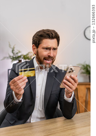 Middle-aged businessman sighs at insufficient funds holding smartphone and credit card about balance Middle-aged businessman sighs at insufficient funds holding smartphone and credit card about balance 132666393