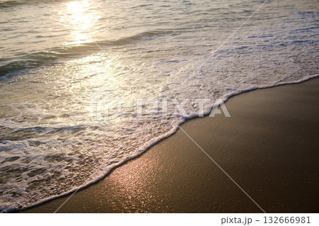 Peaceful ocean waves gently wash over golden sand at sunset, creating a serene and tranquil beach atmosphere with shimmering reflections 132666981