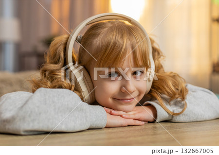 Young girl listening to audiobook with headphones, excitedly reacting to story with open eyes, smile 132667005