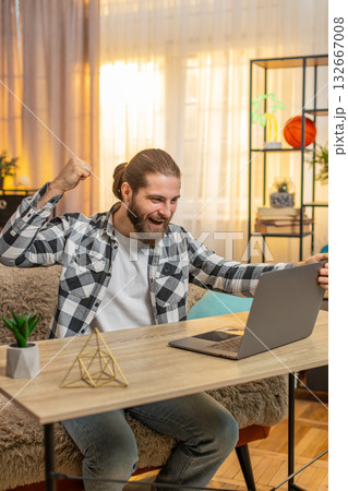 Young man man opens laptop at home wow great winning result in an online course celebrates victory 132667008