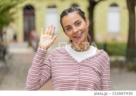 Happy woman smiling friendly at camera waving hands gesturing hello greeting goodbye on city street Happy woman smiling friendly at camera waving hands gesturing hello greeting goodbye on city street 132667430