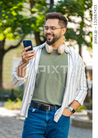 Smiling young man using smartphone typing texting scrolling social media app on city town street 132667433
