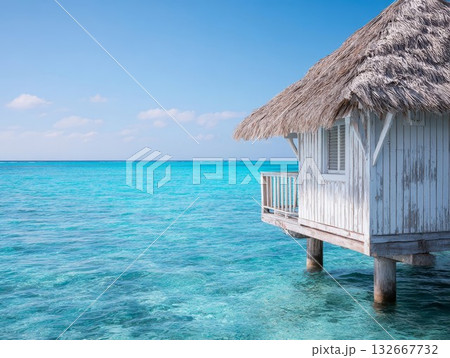 Tropical overwater bungalow with thatched roof sits over turquoise sea on stilts. Clear blue sky and tranquil water provide perfect escape view. Tropical overwater bungalow with thatched roof sits over turquoise sea on stilts. Clear blue sky and tranquil water provide perfect escape view. 132667732