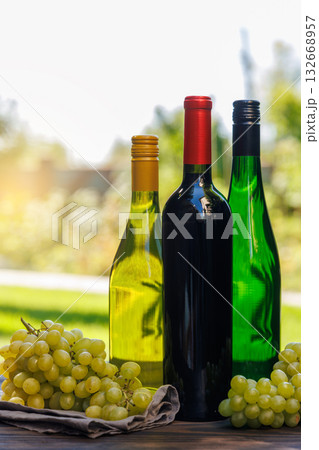 Wine bottles with grapes on a wooden table, glowing with sunny bokeh in the background 132668957