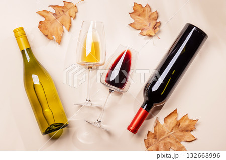Wine glasses and bottles with autumn leaves on beige background Wine glasses and bottles with autumn leaves on beige background 132668996