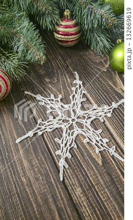 A white crocheted snowflake-shaped doily with fir branches and decorations. 132669619