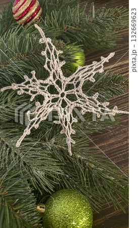 A white crocheted snowflake-shaped doily with fir branches and decorations. A white crocheted snowflake-shaped doily with fir branches and decorations. 132669623