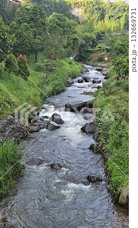 A rapid river with strong currents flows over and around large rocks, creating white water and a small cascade, surrounded by a green. A rapid river with strong currents flows over and around large rocks, creating white water and a small cascade, surrounded by a green. 132669731