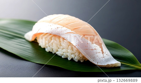 Zen-inspired, a single, perfect nigiri with a slice of yellowtail (hamachi), focusing on the fish's firm texture and clean white fat lines, resting on a bed of green leaf  132669889
