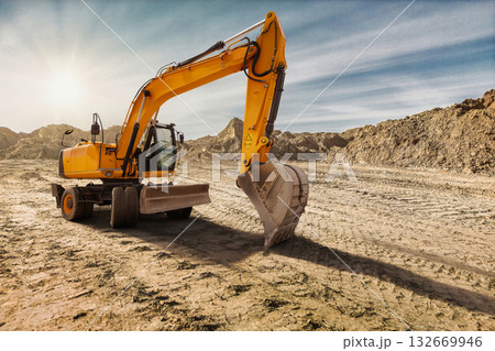 Heavy machinery digs into the dry soil of a construction site. The sun sets, casting warm hues over the landscape and highlighting the excavator's powerful arm Heavy machinery digs into the dry soil of a construction site. The sun sets, casting warm hues over the landscape and highlighting the excavator's powerful arm 132669946