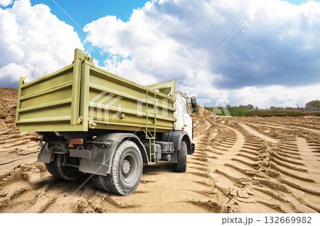 A construction truck stands on a sandy landscape, surrounded by rolling hills and scattered clouds, capturing a moment of hard work and nature's beauty A construction truck stands on a sandy landscape, surrounded by rolling hills and scattered clouds, capturing a moment of hard work and nature's beauty 132669982