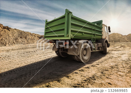 A green dump truck rests on a dirt construction site surrounded by mounds of gravel, basking in the warm glow of the setting sun A green dump truck rests on a dirt construction site surrounded by mounds of gravel, basking in the warm glow of the setting sun 132669985