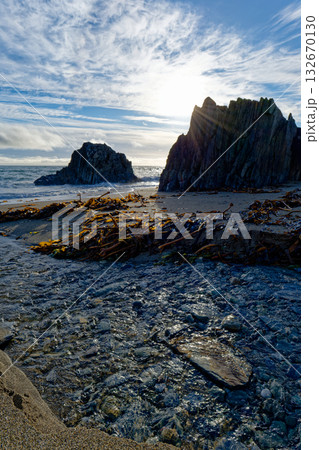Creek flows into ocean at Sheep Cove beach, Ireland, with seaweed scattered along the shore near jagged rocks. Creek flows into ocean at Sheep Cove beach, Ireland, with seaweed scattered along the shore near jagged rocks. 132670130