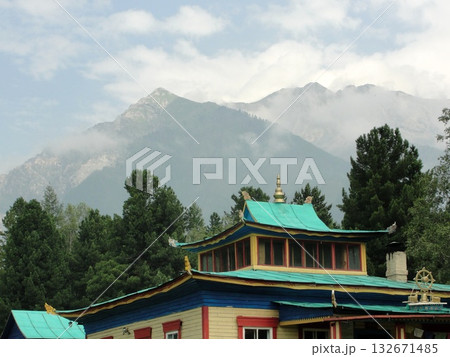 Arshan is a place where nature and architecture harmoniously blend. In the center of the frame stands a traditional building with a bright roof and red accents, surrounded by green trees. 132671485