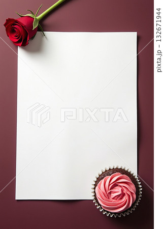 Blank white paper with a red rose and a chocolate cupcake with pink frosting on a burgundy background. Romantic and elegant composition 132671944