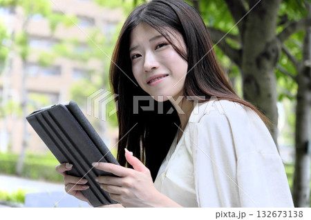 公園の緑の中でタブレットを使う若いビジネスウーマン 公園の緑の中でタブレットを使う若いビジネスウーマン 132673138