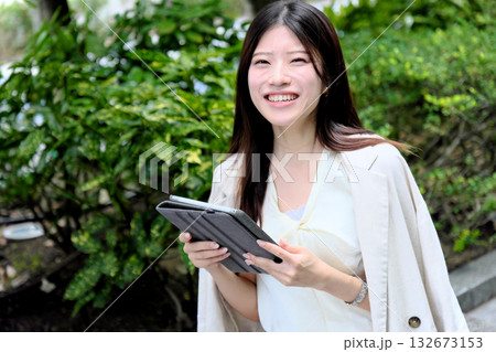公園の緑の中でタブレットを使う若いビジネスウーマン 公園の緑の中でタブレットを使う若いビジネスウーマン 132673153