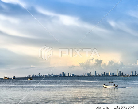 Scenic View of Boats on the Ocean Against a Coastal City Skyline and Soft Evening Sky 132673674