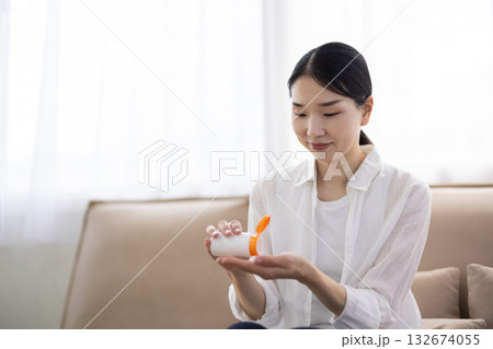 サプリメントをボトルから手のひらに取り出す白シャツのミドル女性 132674055