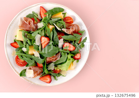 Colorful Italian arugula salad with prosciutto, strawberries, melon, cherry tomatoes, cheese on pink background.Top view Colorful Italian arugula salad with prosciutto, strawberries, melon, cherry tomatoes, cheese on pink background.Top view 132675496