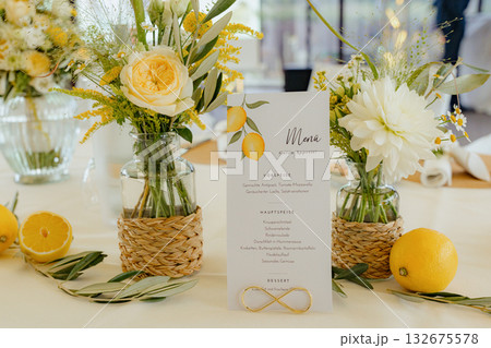 Table setting featuring a menu card with lemons, surrounded by elegant floral arrangements in glass vases. Fresh lemons and greenery add a touch of color and freshness to the table Table setting featuring a menu card with lemons, surrounded by elegant floral arrangements in glass vases. Fresh lemons and greenery add a touch of color and freshness to the table 132675578