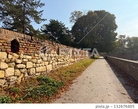 Stone wall and pathway in autumn park. Historical architecture, seasonal atmosphere, and tranquil outdoor perspective. 132676805