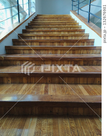 Upward view of glossy wooden stairs with parquet treads, clean architectural interior with symmetry and daylight Upward view of glossy wooden stairs with parquet treads, clean architectural interior with symmetry and daylight 132676981