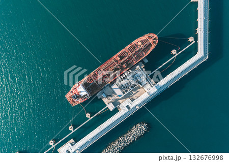 Aerial top down view of a large oil tanker docked at a pier in the port in process of loading. 132676998