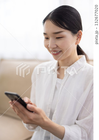 ソファに座ってスマートフォンを操作するミドル女性 ソファに座ってスマートフォンを操作するミドル女性 132677020