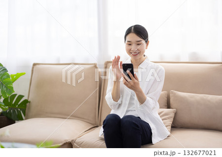 ソファに座りスマートフォンでビデオ通話を楽しむミドル女性 132677021