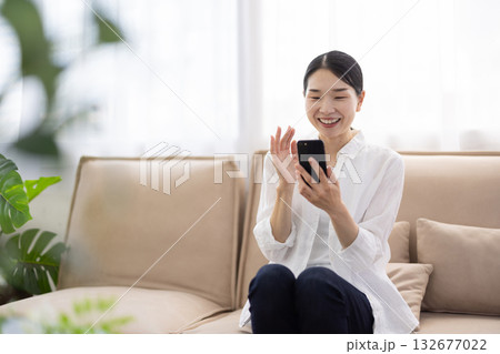 ソファに座りスマートフォンでビデオ通話を楽しむミドル女性 132677022