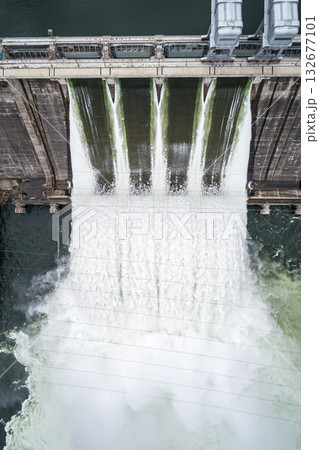 Aerial top down view of concrete dam releasing water into river on cloudy day. Water discharge at hydroelectric power plant. Aerial top down view of concrete dam releasing water into river on cloudy day. Water discharge at hydroelectric power plant. 132677101