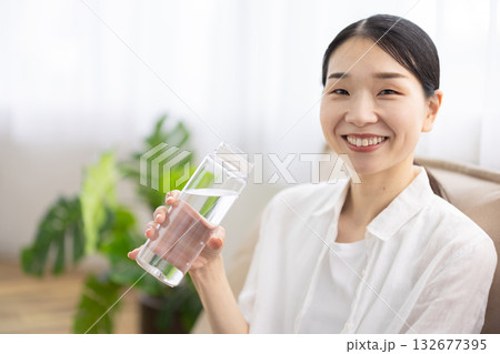 ソファに座り水の入ったボトルを持って微笑むミドル女性 132677395