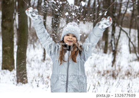 Girl in a silver winter coat throws snow joyfully in a forest setting, capturing carefree outdoor fun 132677689