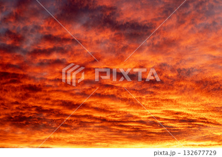 Fiery sunset paints dramatic sky with orange and red clouds over calm horizon Fiery sunset paints dramatic sky with orange and red clouds over calm horizon 132677729