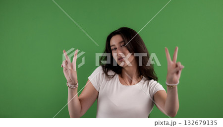 Young woman making peace sign with both hands on green background 132679135