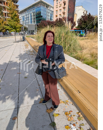Woman with camera standing near urban park on autumn day. Creative profession, lifestyle photography and balance between city life and personal expression. 132679229