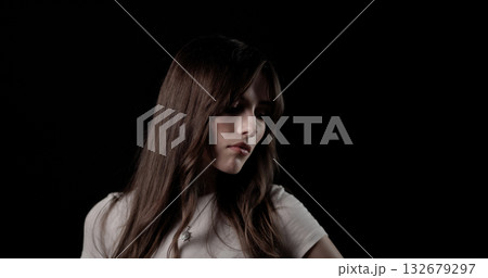 Fashion model with long brown hair wearing white t shirt and necklace looking down on black background 132679297