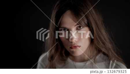Fashion model posing with serious expression and long brown hair on black background Fashion model posing with serious expression and long brown hair on black background 132679325