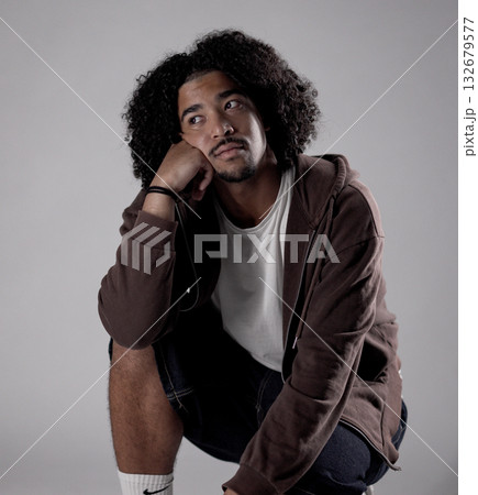Pensive young african-american man crouching and looking away, resting his face on his hand Pensive young african-american man crouching and looking away, resting his face on his hand 132679577